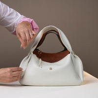 Model holding Aurora Soft Bag in ivory – balloon-shaped leather handbag with pleated sides