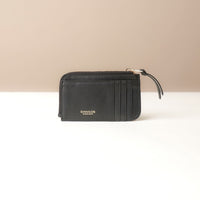 Black card case wallet with a visible brand name on a beige background