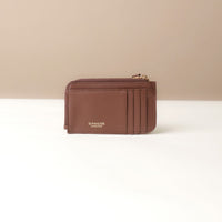 Brown card case wallet with gold zipper on a beige background