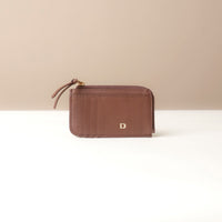 Brown card case wallet with a gold zipper and brand logo on a beige background