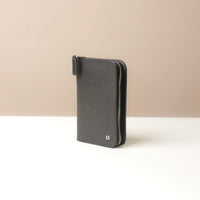 Side view of a black passport case lovable in pebble leather with a Danilos logo on a beige background with zipper