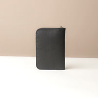 Back view of a black Danilos passport case lovable in pebble leather on a beige background