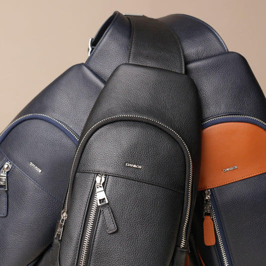 Close-up of three Danilos leather sling packs, Andres' bags with silver zippers on a beige background