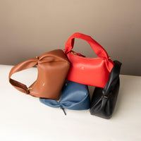 Aurora leather handbags stacked – navy, red, black, and tan sculptural silhouettes