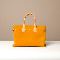 Yellow suede leather danilos  tote bag with tan handles and accents on a beige background