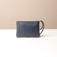 Navy leather wristlet pouch bag with wrist strap on a beige background