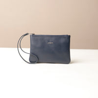 Navy blue leather wristlet pouch bag with a strap on a beige background
