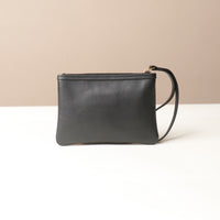 Black leather wristlet pouch with wrist strap on a beige background