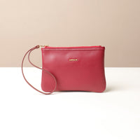 Red leather wristlet pouch bag with a strap on a beige background