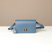 Blue crossbody bag with a gold clasp on a beige background