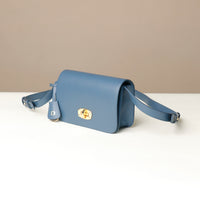 Blue crossbody bag with a gold clasp on a white surface with a beige background