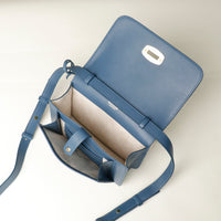 Blue leather crossbody bag opened with a strap on a light beige background