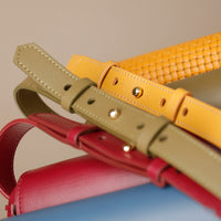 Close-up of three leather belts in red, yellow, and beige on a neutral background.