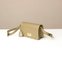 green crossbody bag with a gold clasp on a white surface with a beige background