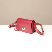 Red crossbody bag with a gold clasp on a white surface with a beige background