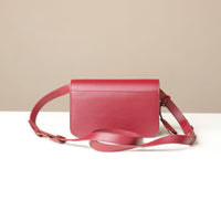 Red leather crossbody bag on a white surface with a beige background