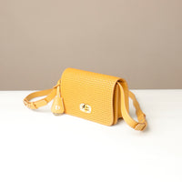 Yellow woven crossbody bag on a white surface with a beige background