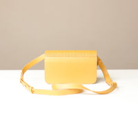 Yellow crossbody bag with a textured top on a white surface and beige background