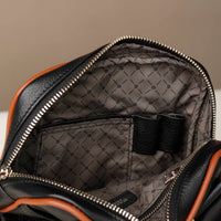 close up  view of a opened danilos black and brown crossbody dylan bag with organizing pockets inside, over a beige background