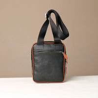 back view of a danilos black and brown crossbody dylan bag with zipper pocket over a beige background