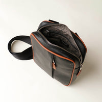 upper view of a open zipper danilos black and brown crossbody dylan bag over a beige background