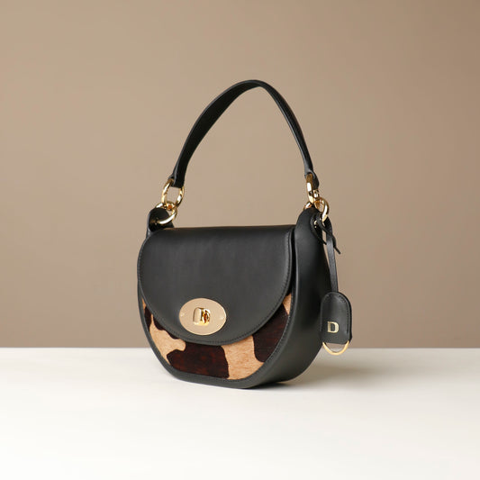 Black Danilos round hair on leather handbag with a gold clasp on a beige background