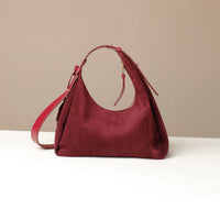red suede leather danilos handbag on a white surface with a beige background