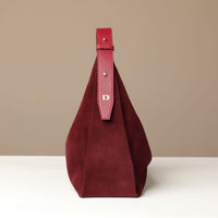 side of a red suede leather danilos handbag with a red strap on a beige background