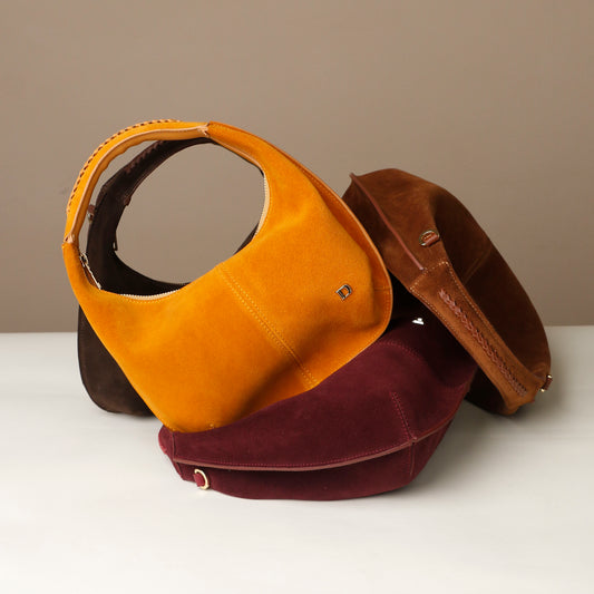 Three suede danilos handbags in brown, yellow, and red on a white surface with a beige background