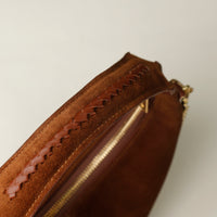 Close-up of a brown suede leather danilos handbag with braided handle on a beige background