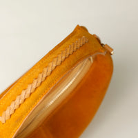 Close-up of a yellow suede leather danilos handbag with braided detail on a light gray background
