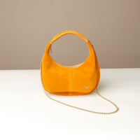 Yellow round suede leather danilos handbag with a chain detail on a white surface and beige background