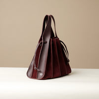 side Front view of burgundy Suede Papillon Sr. – pleated suede bucket handbag with leather trim