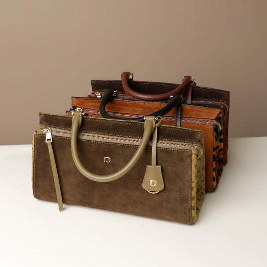 Three leather Danilos handbags stacked on a white surface with a beige background