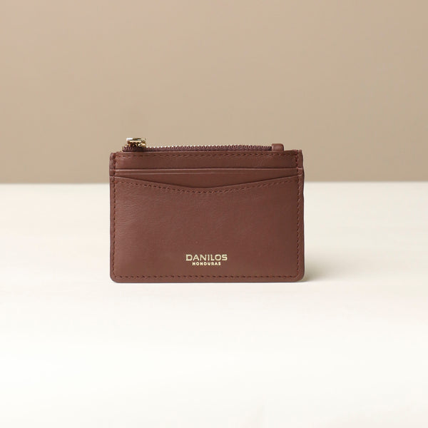 front view of a pebble leather card case nirua in brown with gold accents over a beige background