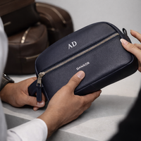 Person holding a navy blue toiletry bag 2014 with 'AD' initials and 'Danilos' branding