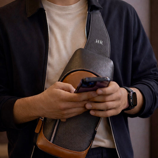 Man holding a black and brown Milano bag with a phone, wearing a dark jacket and white shirt.