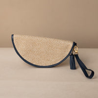 semicircular woven raffia Agnes clutch with navy leather strap and tassel on a beige background