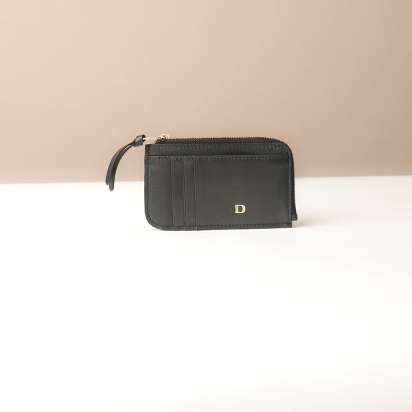Black card case wallet with a gold zipper and brand logo on a beige background