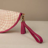 Close-up of a clutch Agnes made with natural fiber and mahenta leather details, with leather strap and tassel, front view