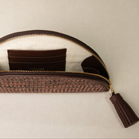 Close-up of a open clutch Agnes made with raffia and palisander, brown leather details, with leather strap and tassel, gold hardware
