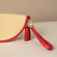 Close-up of a half-circle clutch Agnes made with raffia rot and red leather details, with leather strap and tassel, front view