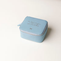 front view of a small leather Danilos Jewelry Organizer Anushka in light blue with embossed text on and a silver zipper, a beige background