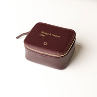 front view of a small leather Danilos Jewelry Organizer Anushka in dark brown with embossed gold text on a white background