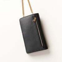 back view of a black danilos leather multi smartphone alessia with a gold zipper pocket and chain over a beige background