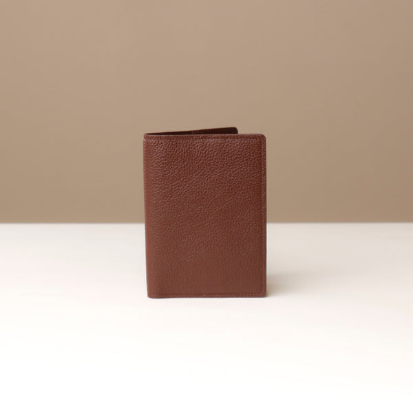 front view of a brown pebble leather passport lovable Danilos on a light surface with a neutral background
