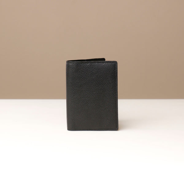 front view of a black pebble leather passport lovable Danilos on a light surface with a neutral background