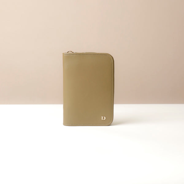 Front view of a green passport case lovable with a Danilos logo on a beige background