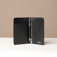 Front view of a open danilos travel pro passport case in black leather lux with 8 card slots a zipper compartment, a pen and 1 passport slot in brown pebble leather in a beige background