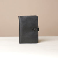 Front view of a black Danilos pebble leather inskspirator with a clip closure on a beige background